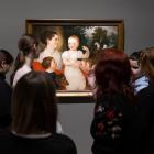 Apmeklētāju grupa muzejā stāv pie sienas un aplūko gleznu ar sievieti un bērniem.