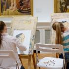 Divas meitenes muzejā sēž pie molbertiem un zīmē portretus, iedvesmojoties no gleznām pie sienas.