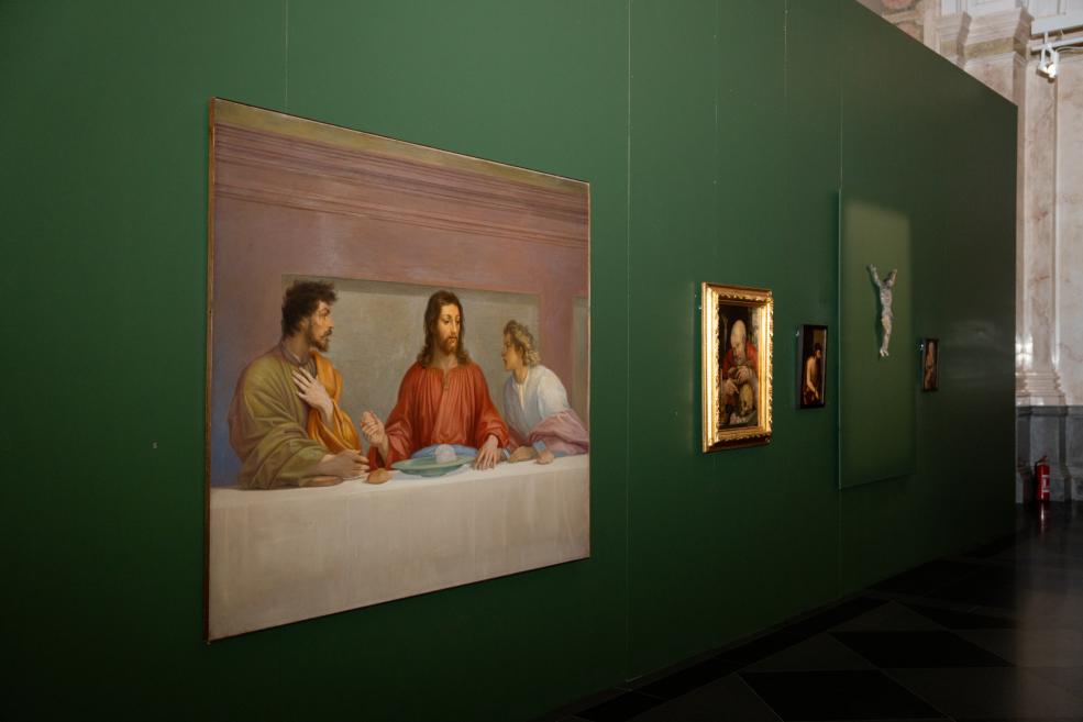 Museum gallery view with a green wall and several hanging artworks, dominated by a large painting of three seated figures at a table.