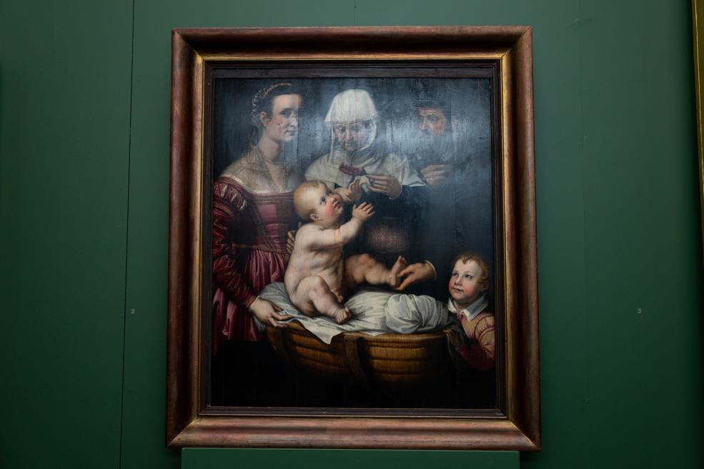 Framed painting of a woman, a man wearing a white headdress, and two children, one seated on a table, in a dark green museum gallery.