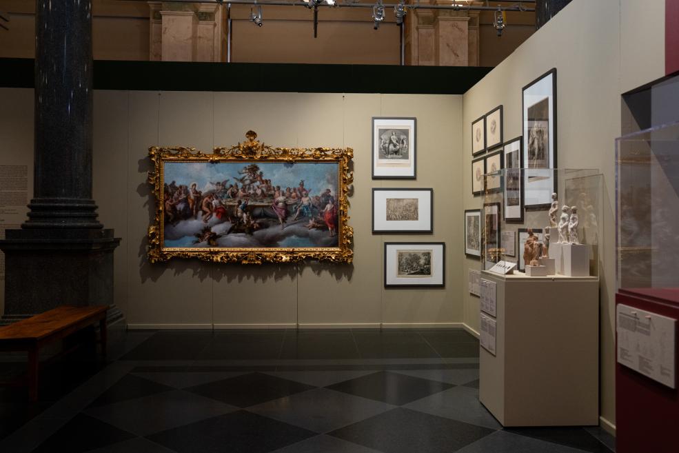 Museum exhibition hall with a large painting in an ornate gilded frame, several prints on the wall, and sculptures in a glass display case.