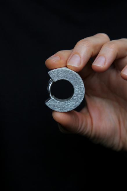 A hand holding a matte metal ring with an open circular shape against a dark background.
