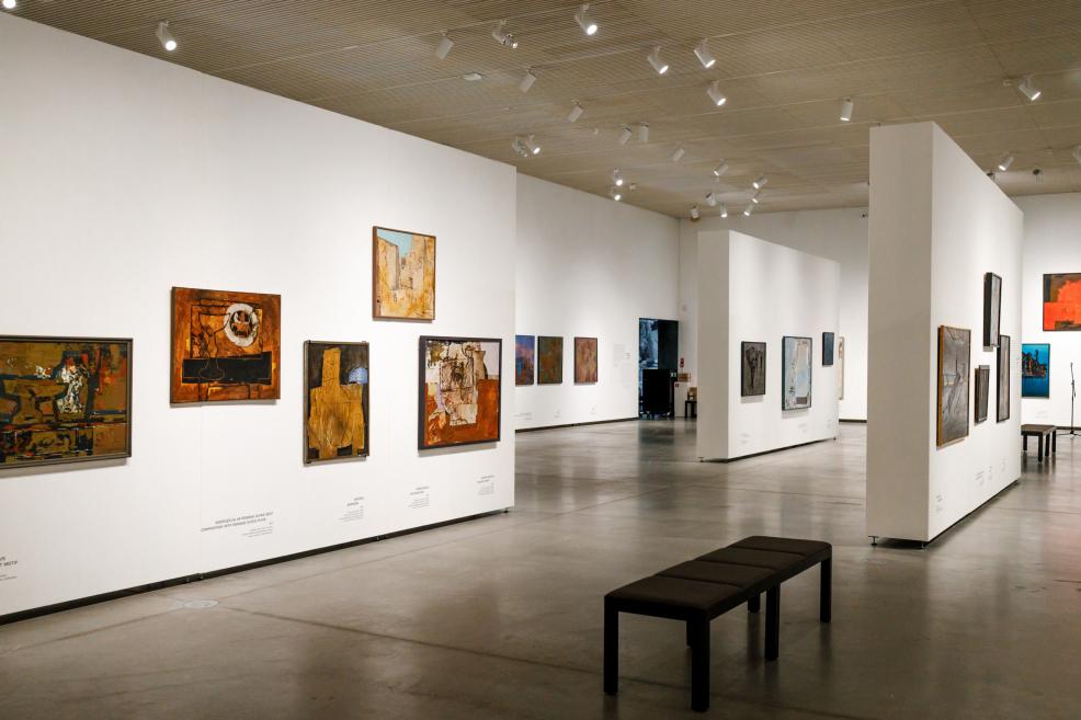 Exhibition view showing paintings by Ojārs Ābols displayed on white partition walls in a spacious, contemporary museum gallery with seating for visitors.