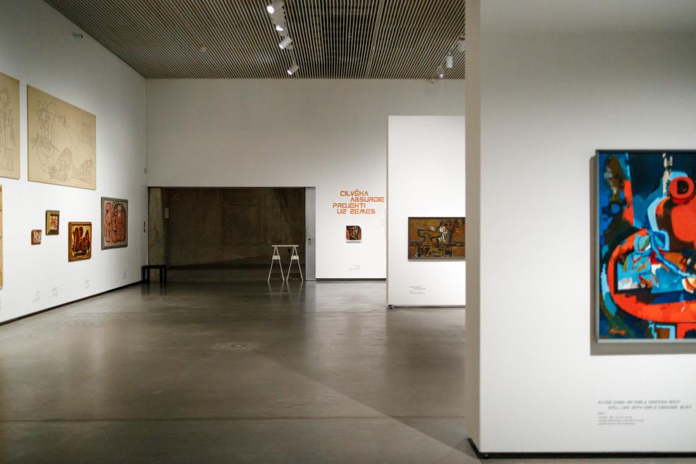 Wide view of the exhibition gallery with works by Ojārs Ābols displayed on white walls, showing the spatial layout, partition walls, and the exhibition title on the wall.