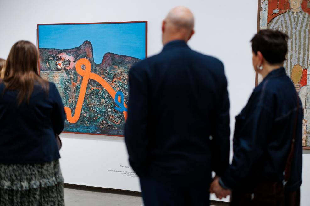 Exhibition visitors seen from behind viewing a painting by Ojārs Ābols with a bright blue background and an orange linear abstract motif, displayed on a white gallery wall.