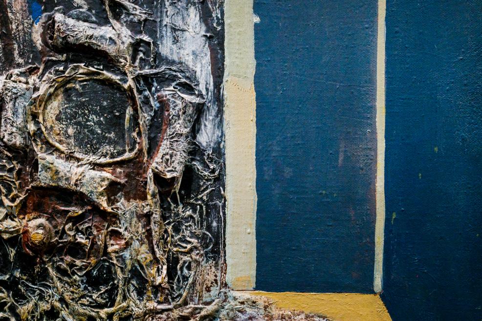 An abstract painting with a strongly textured surface, featuring thick, relief-like layers of paint on the left and calm blue and beige color bands with clear, geometric edges on the right.