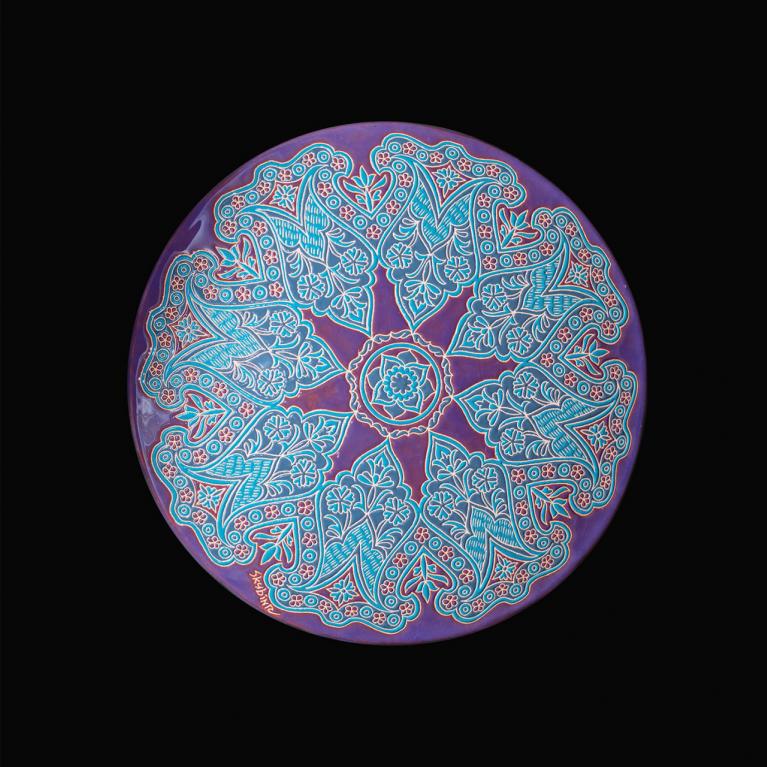 Round decorative plate with an intricate blue and red pattern on a violet-pink background.