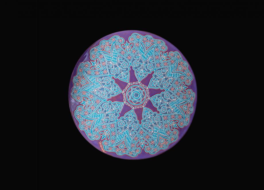 Round decorative plate with an intricate blue and red pattern on a violet-pink background.