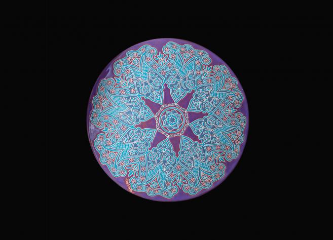 Round decorative plate with an intricate blue and red pattern on a violet-pink background.