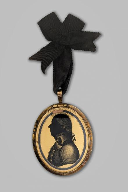 Ovāls portreta medaljons ar vīrieša profila siluetu zeltītā ietvarā, pie kura piestiprināta melna lente.