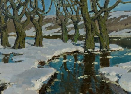 Ziemas ainava ar kailiem kokiem pie ūdensmalas, kur sniegs un koku atspulgi veido kontrastu uz zilā debesu fona.