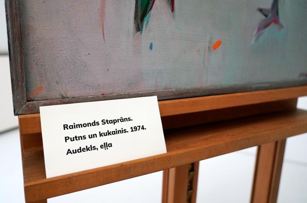 Raimonda Staprāna 1974. gada glezna Putns un kukainis uz koka statīva ar muzeja etiķeti priekšā.