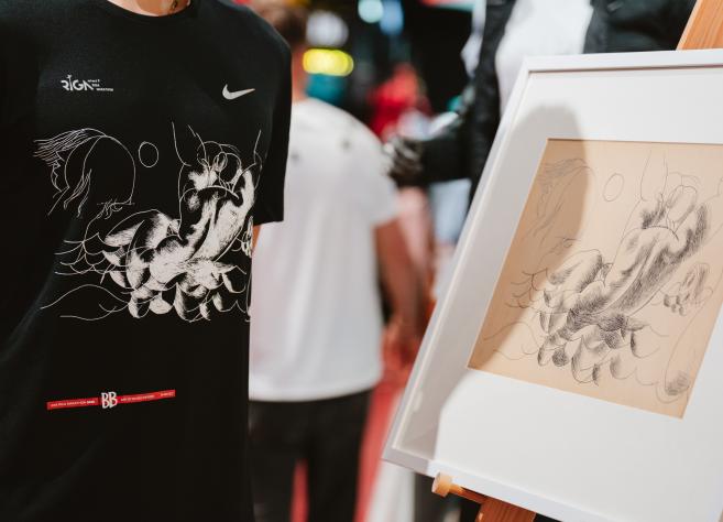 Mākslas darbs ar zīmējumu, kuram blakus ir krekls, kurā attēlots šis zīmējums