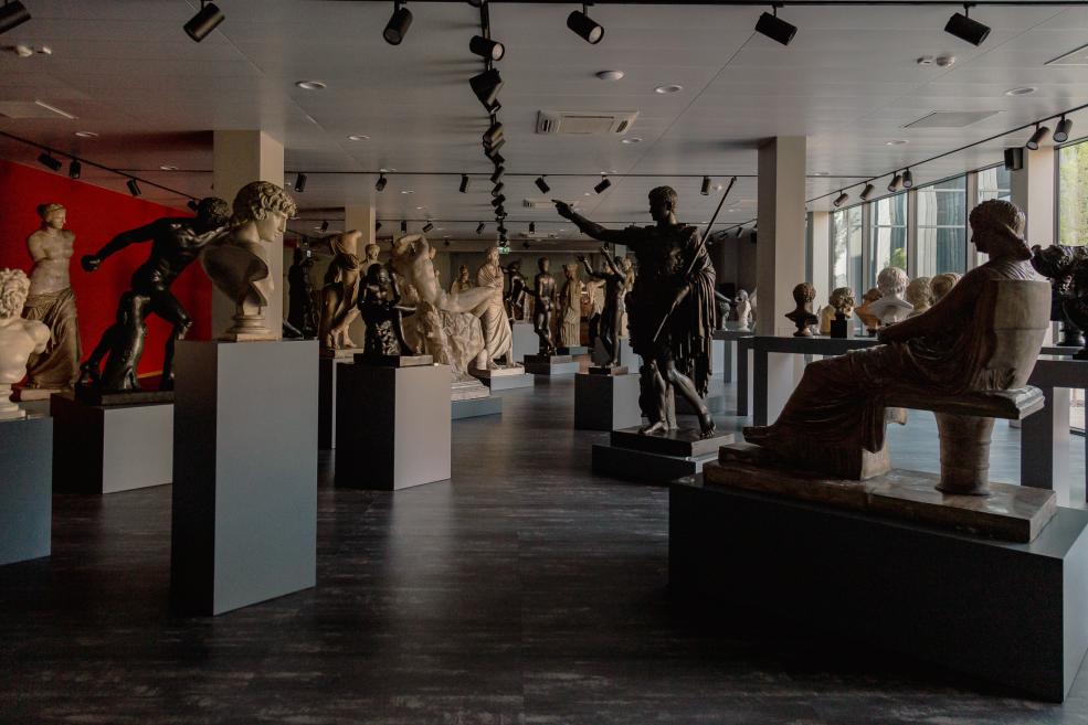 Plaša muzeja skulptūru zāle ar klasiskām statujām uz postamentiem un apgaismojumu no griestiem.