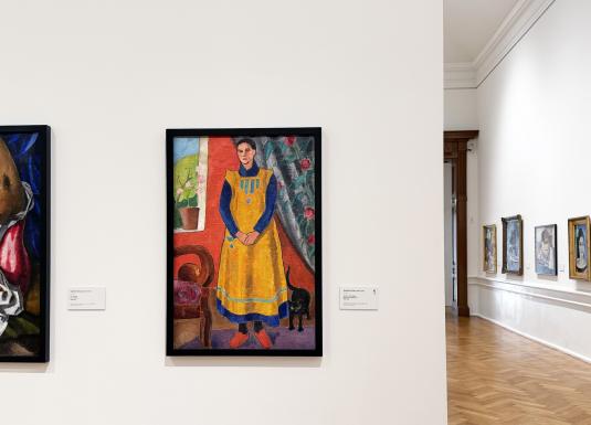 Muzeja interjerā redzama gleznu ekspozīcija uz baltas sienas ar dažādiem darbiem rāmjos.