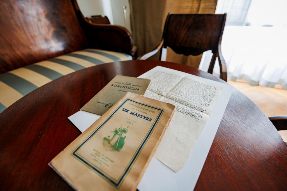 Uz koka galda muzeja interjerā novietotas vecas grāmatas un dokumenti, fonā redzamas klasiskas mēbeles.