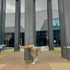 Trīs jaunieši pie muzeja ēkas kolonnām izpilda līdzsvara pozu ar izstieptām kājām un rokām.