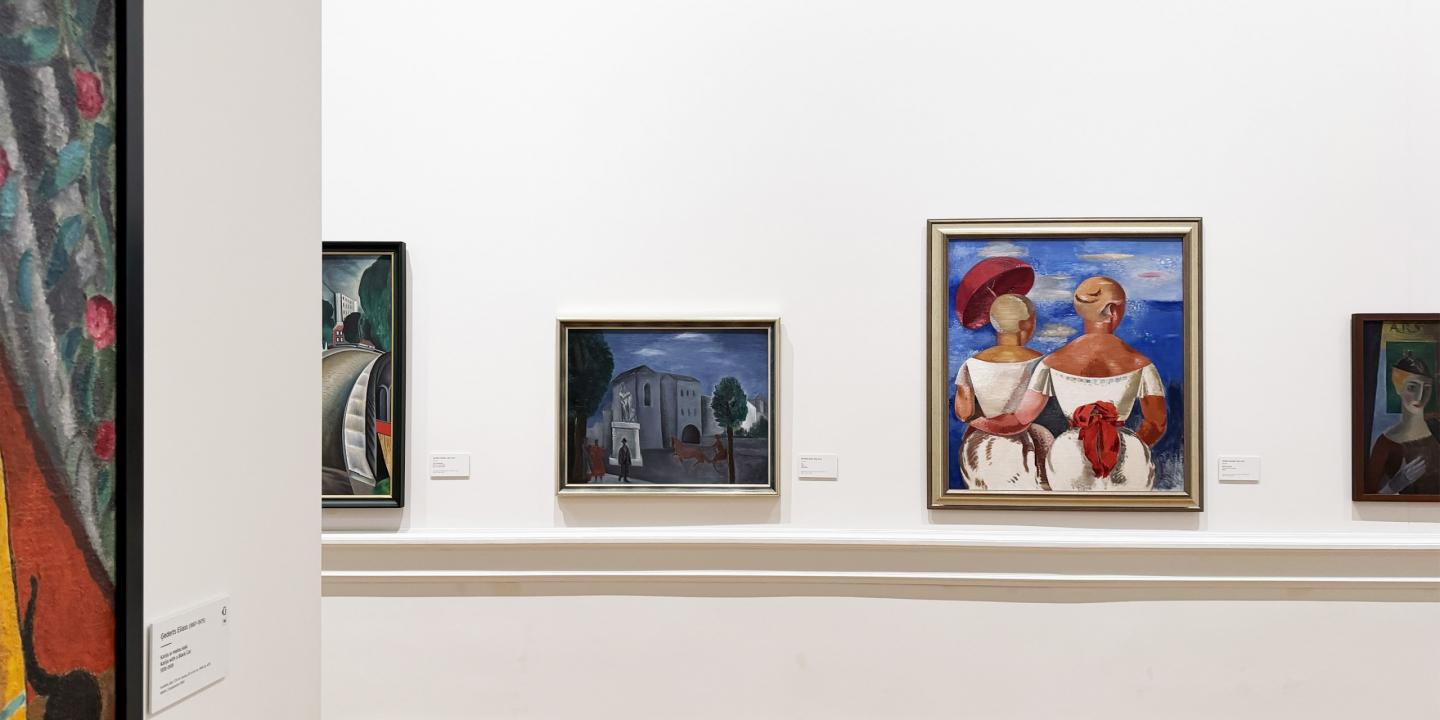 Muzeja sienā izkārtotas vairākas gleznas, tostarp ainava un divu figūru kompozīcija spilgtās krāsās.