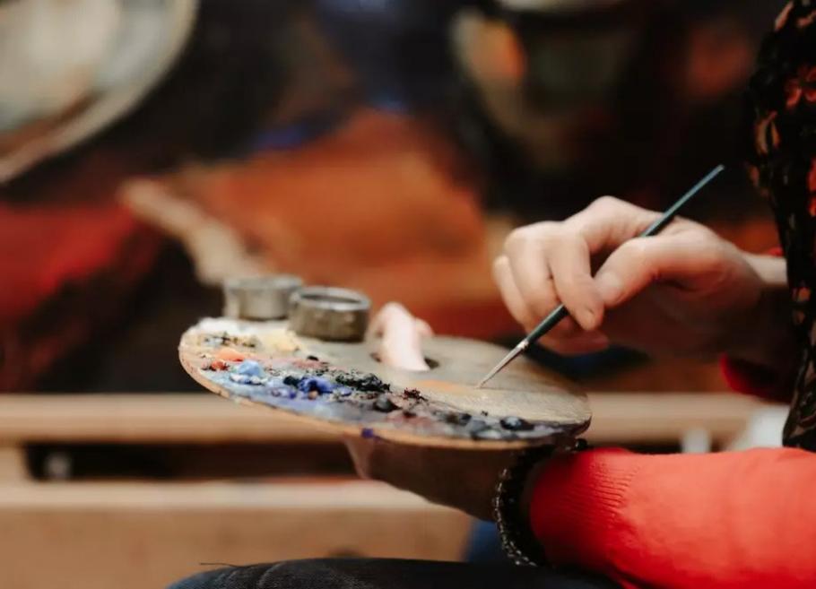 A person painting with a brush while holding a paint palette.