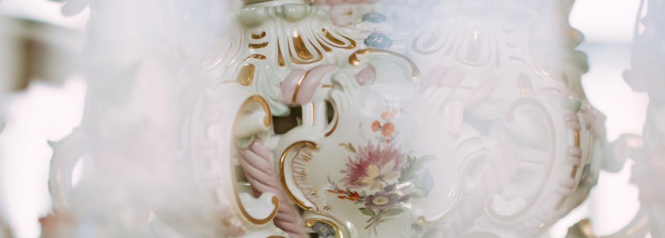 Detail of a decorative porcelain vessel with floral ornament and gilded decorative lines.