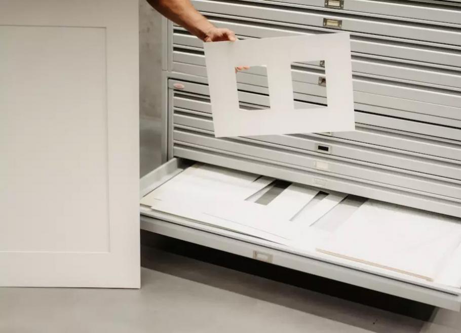 A person removing a sheet with graphic works from a museum storage drawer.