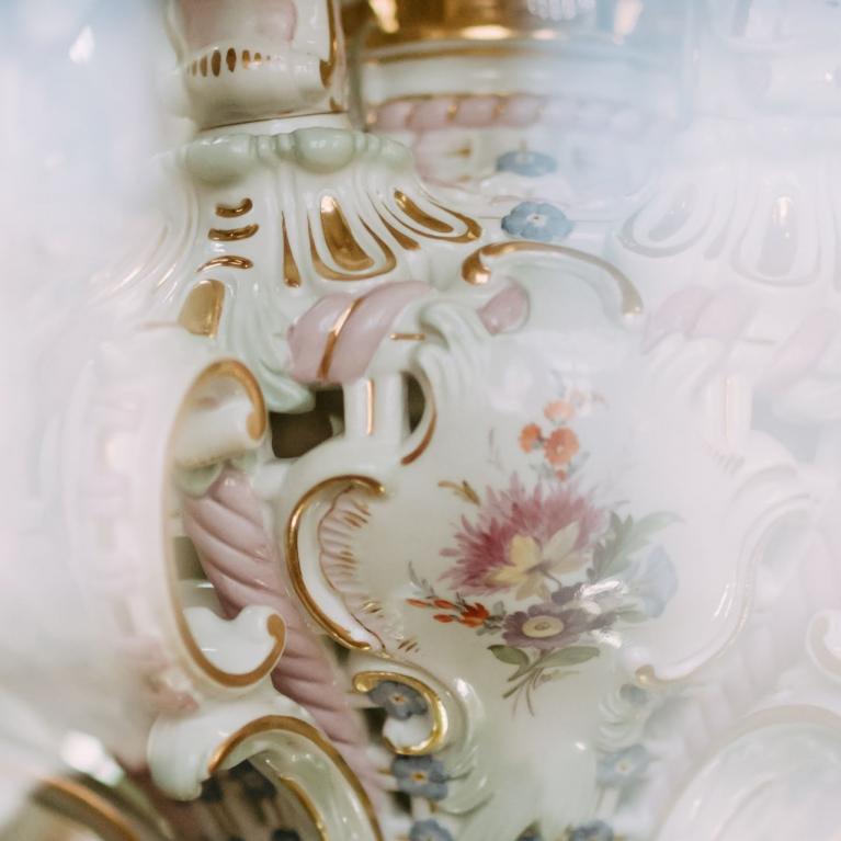 Detail of a decorative porcelain vessel with floral ornament and gilded decorative lines.