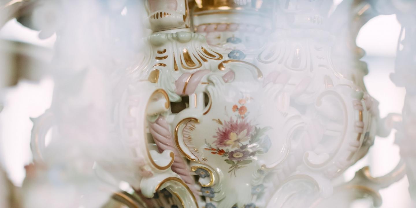 Dekoratīva porcelāna trauka detaļa ar ziedu ornamentu un zeltītām dekoratīvām līnijām.