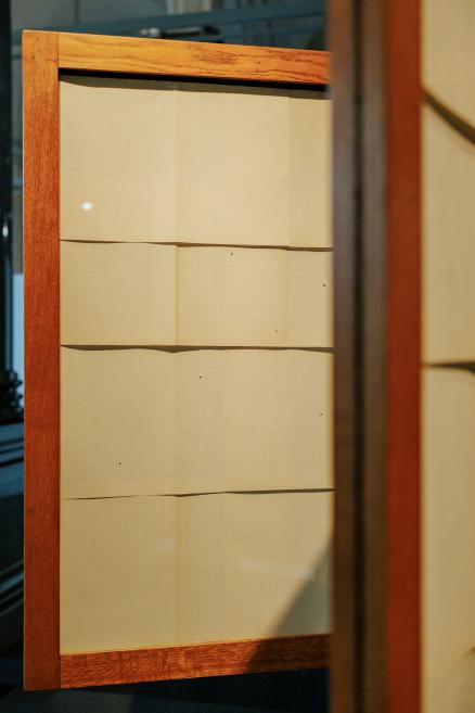 A minimalist installation of light horizontal panels within a wooden frame is shown in close-up as part of a museum exhibition display.
