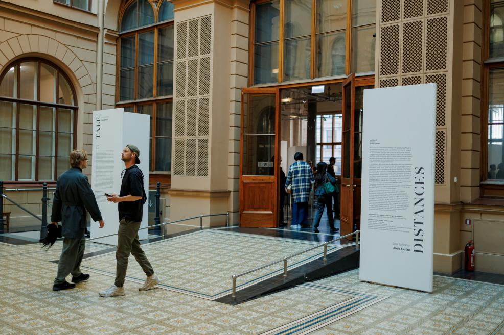 In the museum foyer near the exhibition entrance, visitors move between informational panels displaying the exhibition title and descriptive texts.