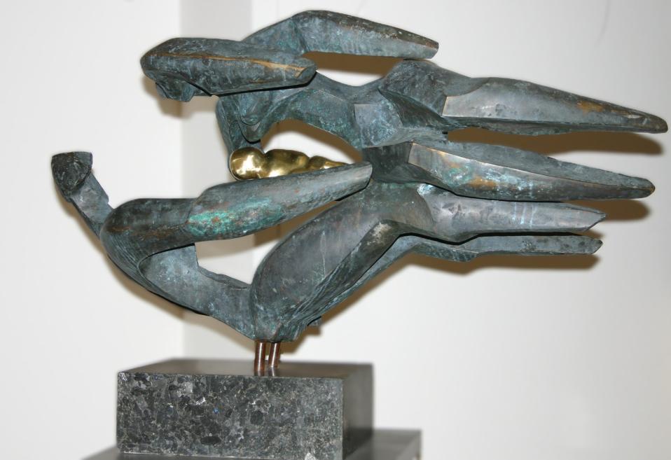 Abstract bronze sculpture with elongated, angular forms on a dark stone pedestal.