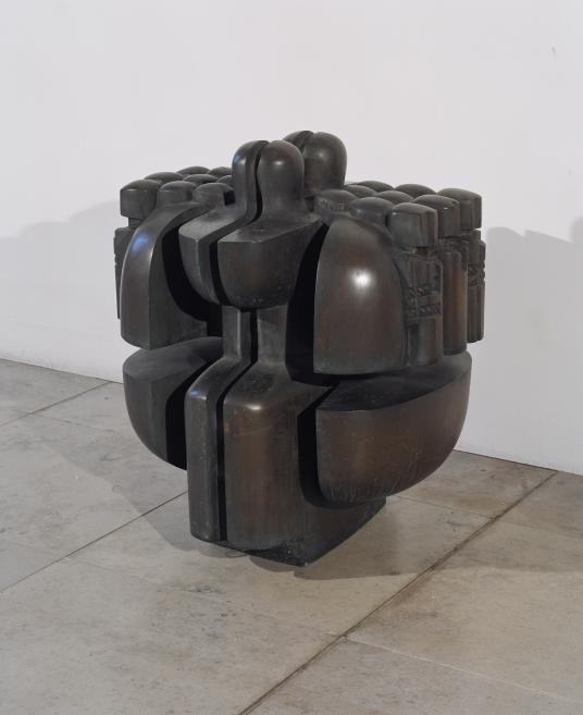 Abstract sculpture of dark metal with rounded interlocking forms in a gallery space on a concrete floor.