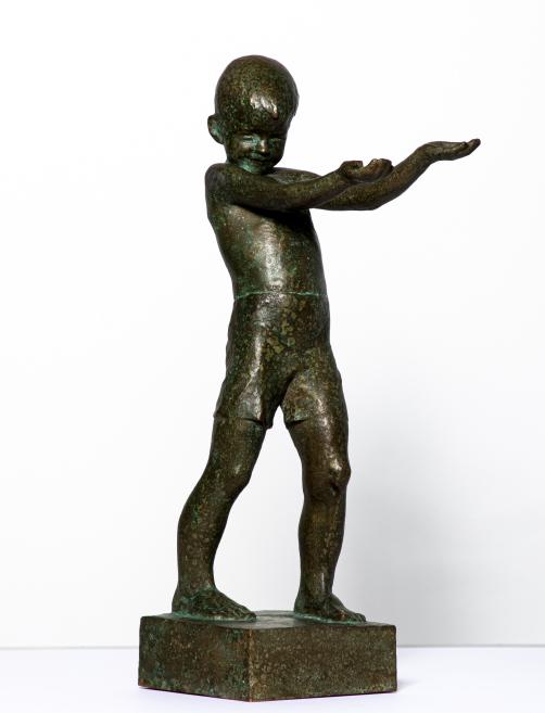 Bronze sculpture depicting a small boy with a large head, outstretched arms, and standing on a rectangular base.