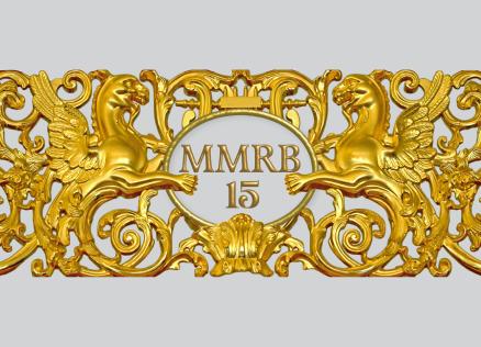 Zeltīts dekoratīvs ornaments ar diviem spārnotiem grifiem, vīnogu ķekariem un centrālu medaljonu ar uzrakstu “MMRB 15”.