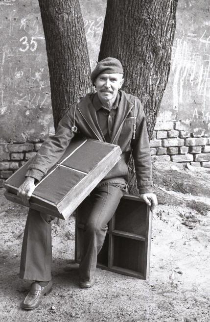 Black-and-white photograph of the artist sitting by a tree holding a large painting.