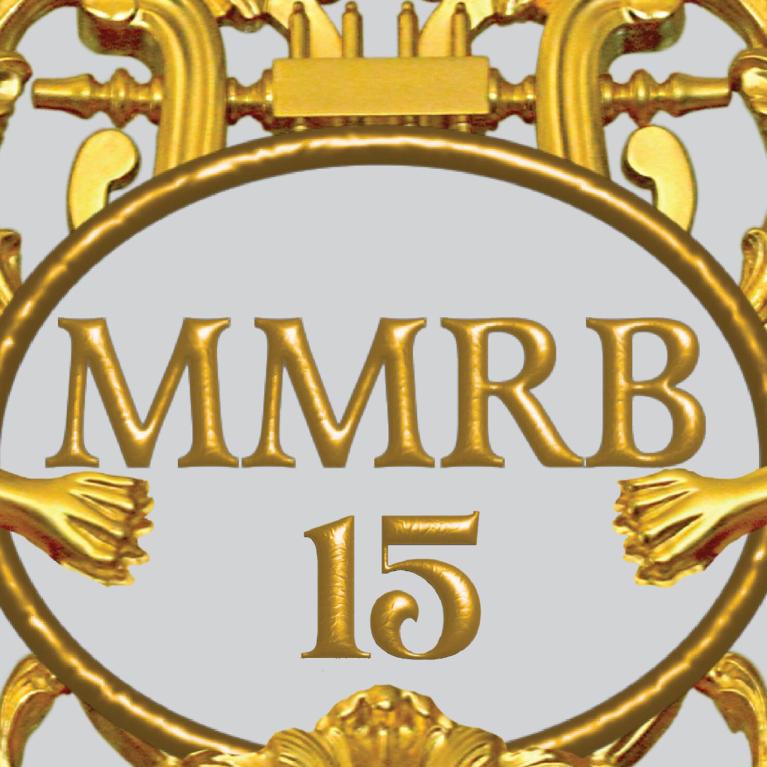 Zeltīts dekoratīvs ornaments ar diviem spārnotiem grifiem, vīnogu ķekariem un centrālu medaljonu ar uzrakstu “MMRB 15”.