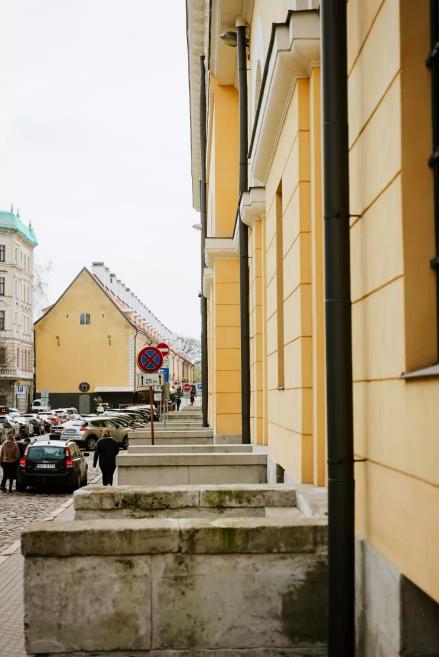 View of the side façade of the Riga Arsenāls building with yellow walls and cars on the street.