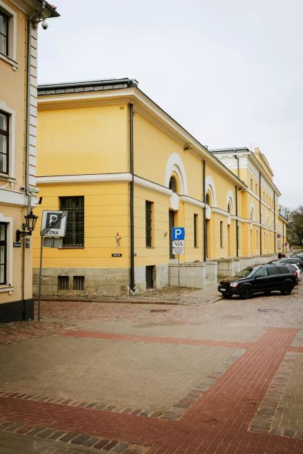The Riga Arsenāls building with yellow walls and white accents seen on a street corner.