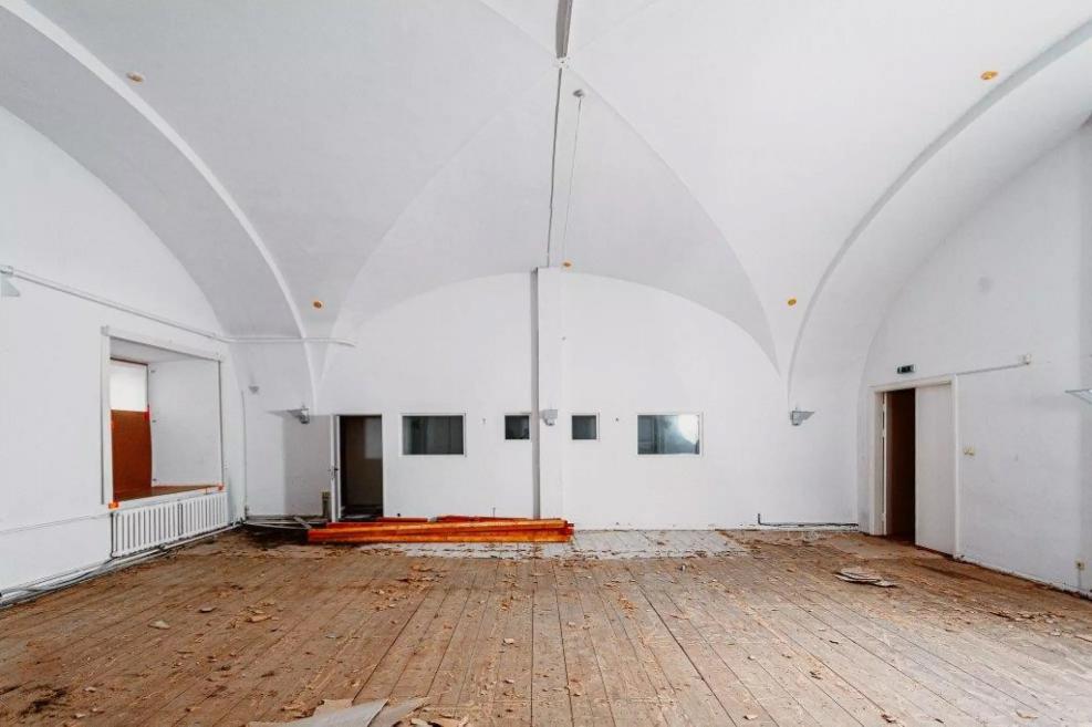 A spacious room with white vaulted ceilings and a worn wooden floor in Riga Arsenāls.
