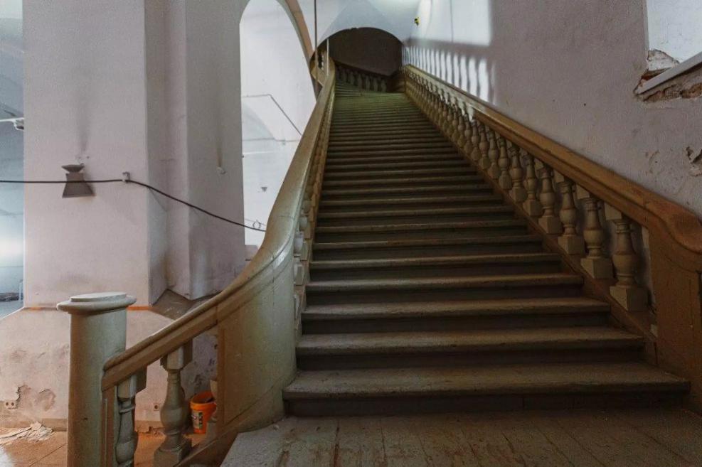A wide staircase with wooden railings leading upward inside the Arsenāls.