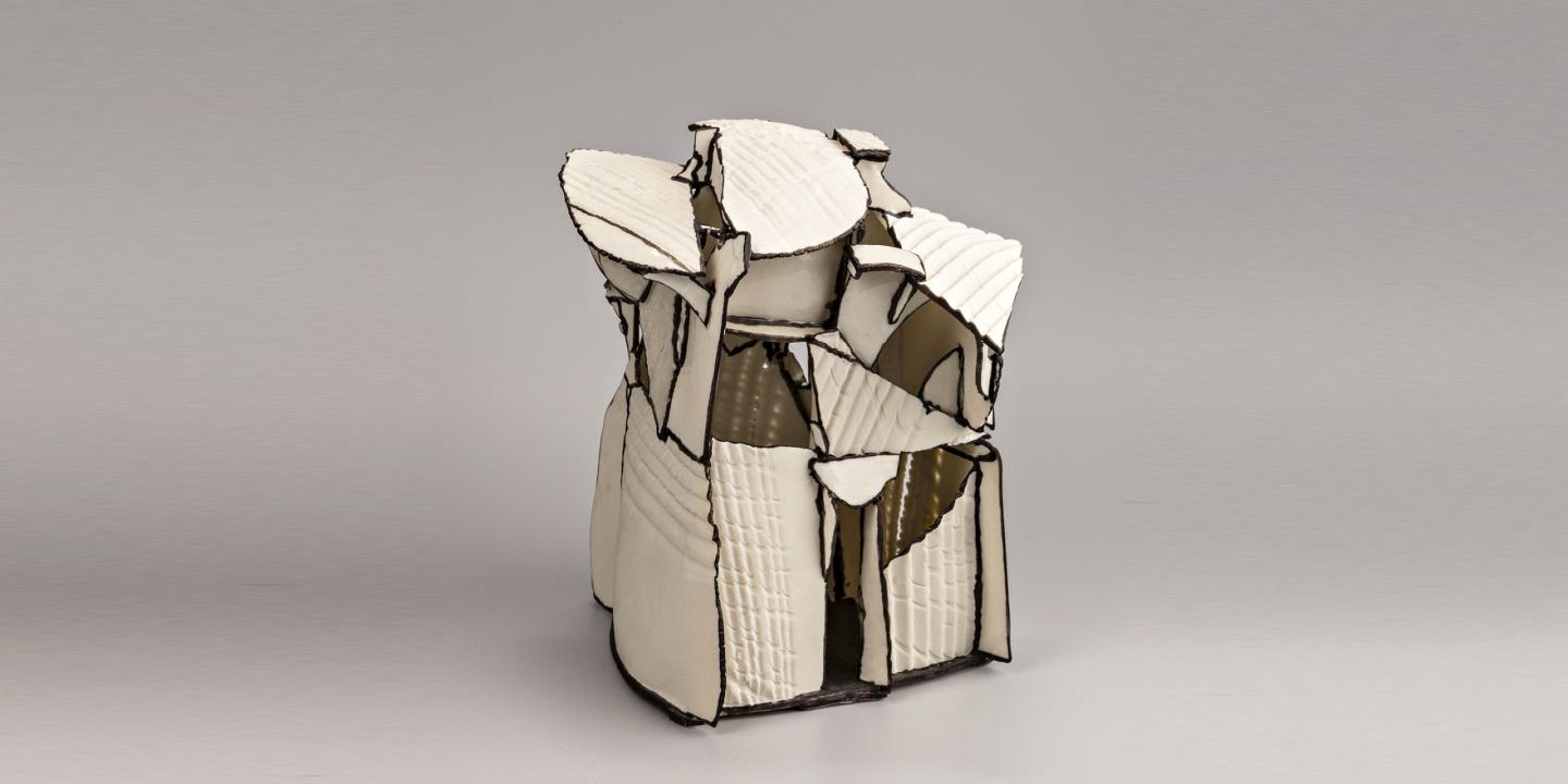 White ceramic sculpture with irregular, faceted plates on a grey background.