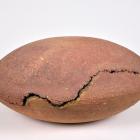 Oval-shaped clay vessel with cracks and a rough surface on a neutral background.