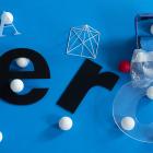 Various typographic forms, geometric objects, and white balls are arranged in an abstract composition against a bright blue background.
