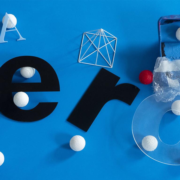 Various typographic forms, geometric objects, and white balls are arranged in an abstract composition against a bright blue background.