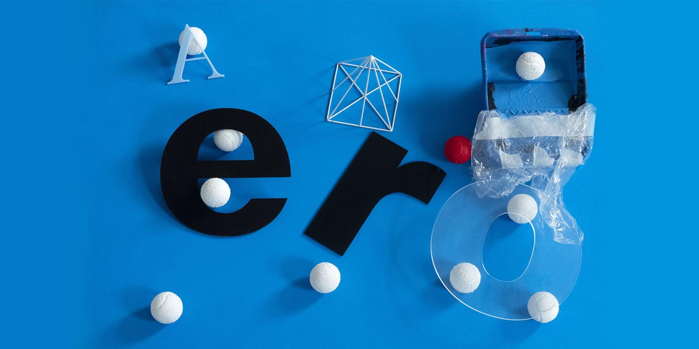 Various typographic forms, geometric objects, and white balls are arranged in an abstract composition against a bright blue background.