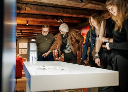 Trīs cilvēki aplūko priekšmetus baltā vitrīnā