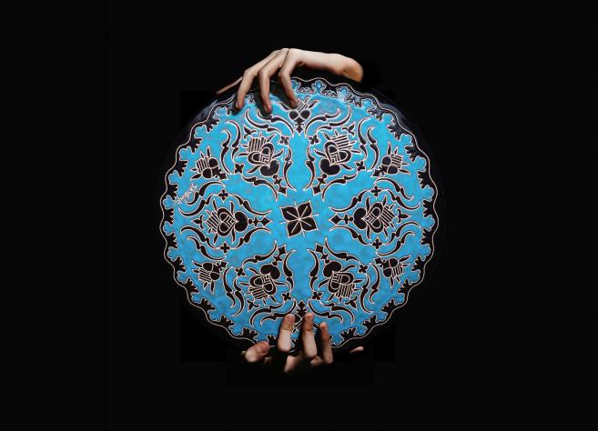 Roku turēta apaļa, zilā krāsā dekorēta keramikas plate ar melniem ornamentiem uz melna fona.