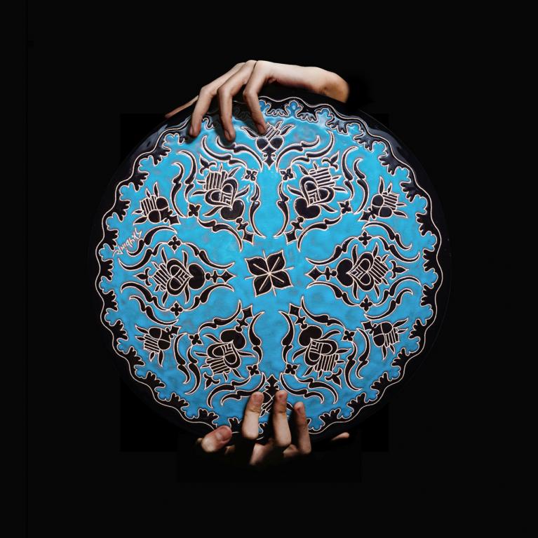 Roku turēta apaļa, zilā krāsā dekorēta keramikas plate ar melniem ornamentiem uz melna fona.