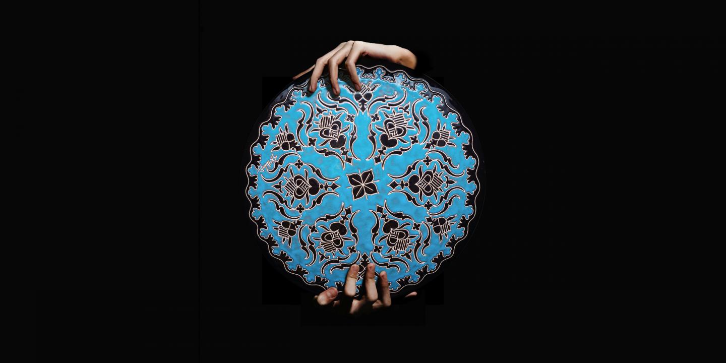 Roku turēta apaļa, zilā krāsā dekorēta keramikas plate ar melniem ornamentiem uz melna fona.