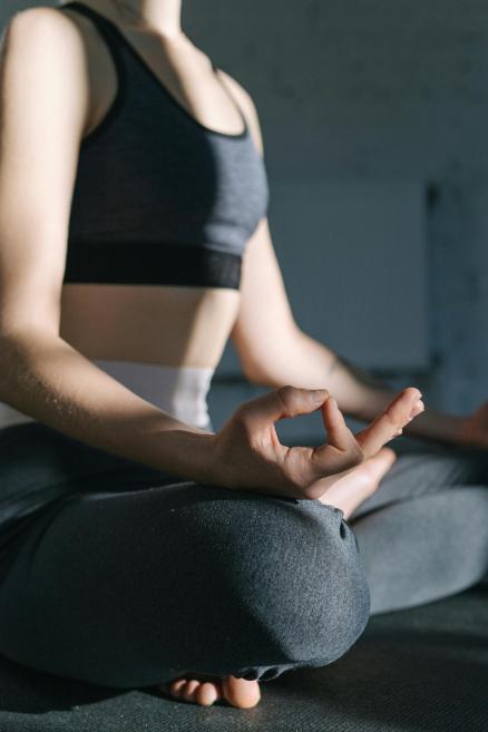 Persona sēž sakrustotām kājām meditācijas pozā, tur rokā mudru un ir tērpta sporta apģērbā.