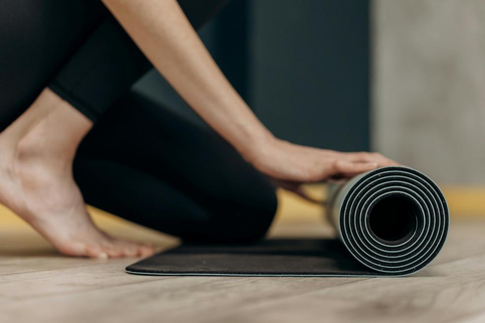 A person sits cross-legged in a meditation pose, holding a hand mudra and wearing athletic clothing.
